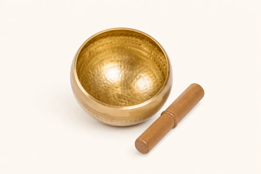 Nadam 8 cm hammered brass singing bowl with its wooden mallet on a cream background